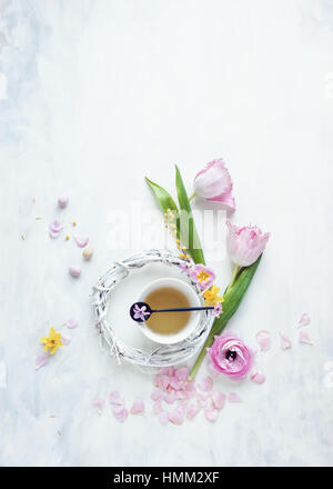 flache Lay Stillleben von Tulpen und anderen Frühlingsblumen mit weißen Kranz Teetasse und Mini Eiern auf weißen und grauen Hintergrund gestylt Stockfoto