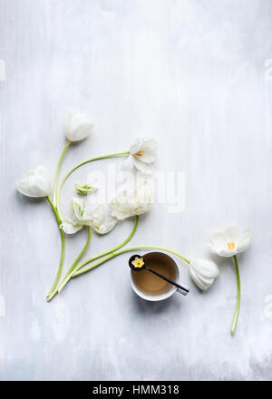 Stillleben mit weißen Tulpen und Teetasse angeordnet und in einem flachen lag über einer gemalten grauen Hintergrund gestylt Stockfoto