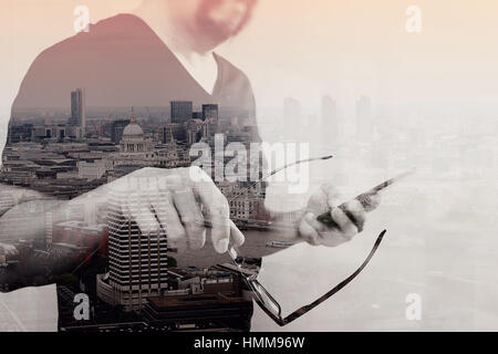 Doppelbelichtung von Designer-Hand mit Brillen, mit Smartphone, London Architektur Stadt Stockfoto