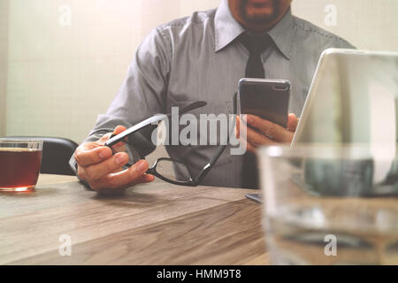 Erfolg Geschäftsmann Hand mit Brillen, Smartphone, Digital tablet Docking-smart-Tastatur auf Holz Schreibtisch Stockfoto