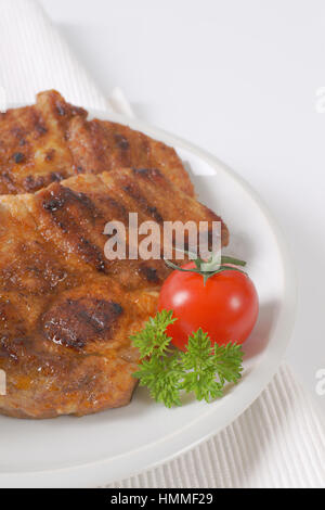 zwei Scheiben gegrilltes Schweinefleisch auf weißen Teller Stockfoto