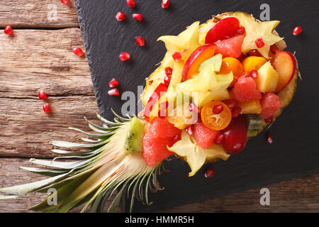 Salat mit tropischen Früchten auf einem Teller mit Ananas-close-up auf dem Tisch. Horizontale Ansicht von oben Stockfoto