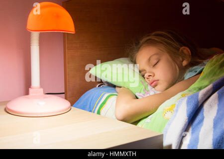 Siebenjährige Mädchen schlafend im Bett, Leselampe ist auf der nächsten Tabelle enthalten. Stockfoto