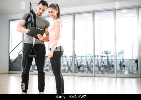 Persönlicher Trainer zeigt Ergebnis der Trainingsplan an seinen weiblichen jungen Klienten mit Aussetzung Seil über die Schulter. Stockfoto