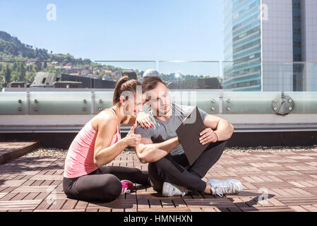 Jungen Erwachsenen persönlichen Fitness-Trainer (Coach) zeigt Ergebnisse und Erfolge, seine jungen weiblichen Kunden auf auf dem Dach des Gebäudes im städtischen Zentrum. Stockfoto