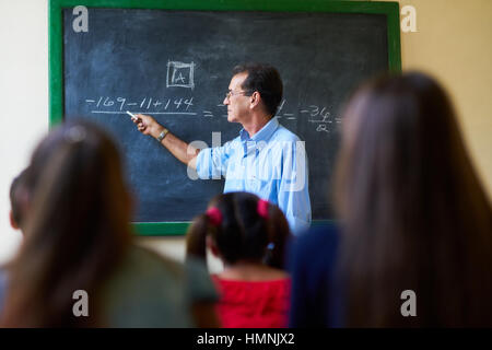 Jugend und Bildung. Gruppe von hispanic Studenten in der Klasse in der Schule während der Lektion. Lehrer an der Tafel erklären Mathematik im Mittelpunkt. Stockfoto