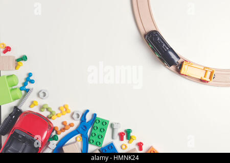 Bunte Kinderspielzeug: Spielzeug aus Plastik Werkzeuge, Schrauben, Muttern, Auto, Bahn, Würfel, Ziegel mit hölzernen Schienen auf weißem Hintergrund als Rahmen mit textfreiraum für Text. Flach zu legen. Ansicht von oben. Getönten Bild Stockfoto