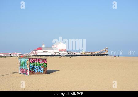 Great Yarmouth Norfolk, Großbritannien - 25. Oktober 2016: Liegestuhl mieten Hütte am Strand bei Great Yarmouth mit Vergnügen Pier im Hintergrund Stockfoto