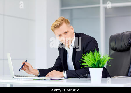 Ernster blonde Mann denkt vor einen Laptop an seinem Schreibtisch die Stockfoto