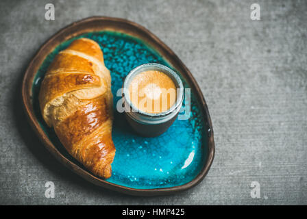 Espressokaffee und Croissant in Türkis Blau Keramik Schale über graue konkreten Hintergrund, Tiefenschärfe, Textfreiraum Stockfoto