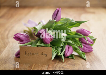 Bouquet von violette Tulpen auf Holztisch mit Mütter-Tageskarte-Papier Stockfoto