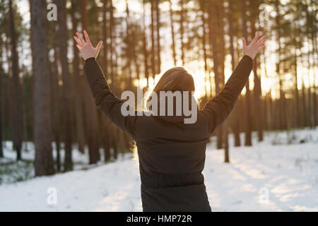 Teen Mädchen hob Hände von hinten im Kiefer Winterwald im Sonnenuntergang Stockfoto