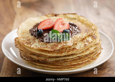 frische Blinis oder Crepes mit geschmolzener Zartbitterschokolade und Beeren Stockfoto