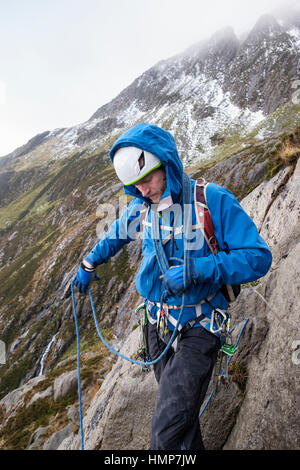 Ein Kletterer, wickeln ein Kletterseil um seinen Körper bereitet sich eine Gerangel in Cwm Idwal, Ogwen, Snowdonia, North Wales, UK, Großbritannien führen. Stockfoto