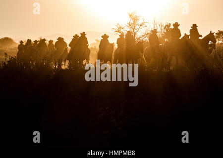 Hunderte von mexikanischen Cowboys sind von der aufgehenden Sonne während der jährlichen Wallfahrt Cabalgata de Cristo Rey 5. Januar 2017 in San José del Rodeo, Guanajuato, Mexiko Silhouette. Tausende von mexikanischen Cowboys und Pferd beteiligen sich die drei-Tages-Fahrt zum Berggipfel Schrein des Cristo Rey stoppen auf dem Weg an Schreinen und Kirchen. Stockfoto