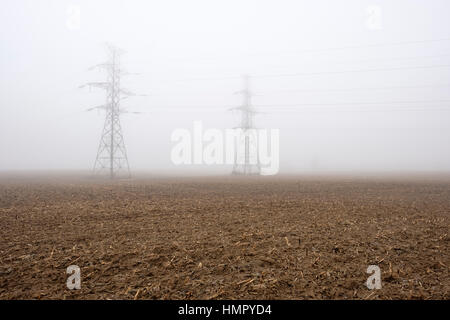 Zwei power-Line-Türme / Pylone auf einem Bauernhof Feld unter dichtem Nebel in Südwest-Ontario, Kanada. Stockfoto