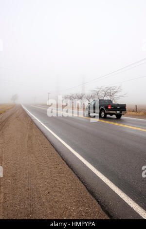 Ein schwarzen Pickup-Truck fährt auf eine asphaltierte Landstraße in einem nebligen Morgen in Südwest-Ontario, Kanada. Stockfoto