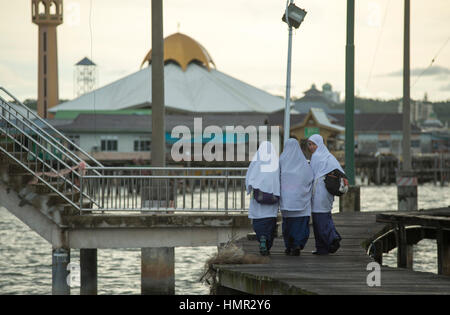 Drei muslimische Mädchen sind auf dem Heimweg von der Schulbildung und überqueren das Wasser auf dem Weg in der Siedlung des Wasserdorfes Kampong Ayer in Bandar Seri Begawan, Brunei. © Time-Snaps Stockfoto