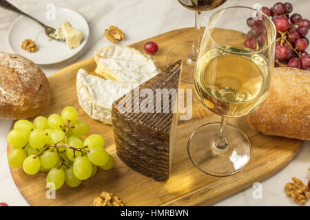 Ein Foto von einem Glas Weißwein mit Käse, Weiß und Roggenbrot, rote und weiße Trauben und Walnüssen, an einem Wein Stockfoto