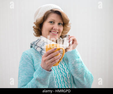 Frau in Pullover, Mütze und Schal mit gelben Tasse Tee Stockfoto