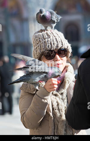 Tauben auf weibliche Touristen nach dem Essen am Markusplatz, Venedig, Italien im Januar Stockfoto