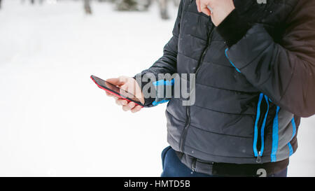 ein junger Mann mit einem Bart, raucht eine elektronische Zigarette und glücklich das Telefonieren über das Internet, eine positive entspannen im Freien in der sn Stockfoto