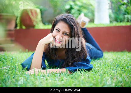 junges Latina Mädchen auf dem grünen Rasen verlegen lächelnd Stockfoto