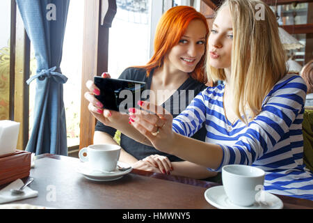 Freundschaft und Technologie. Zwei hübsche Mädchen mit Smartphones beim Tee im Café trinken. Stockfoto