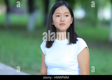 Mädchen weibliche Teenager mit schwarzen Haaren in einem Bob weiße ostasiatischen Frau grüne Park Hintergrund. Dame mit Platte und drückt einen Finger lächelnd, auf der Suche Stockfoto
