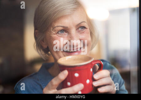 Ältere Frau am Fenster hält eine Tasse Kaffee Stockfoto