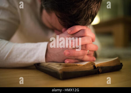 Nicht erkennbare Mann, der betet, kniend auf dem Boden, die Hände auf Bibl Stockfoto