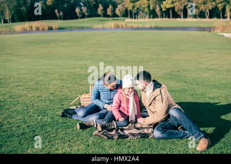 Schöne Familie sitzt auf der grünen Wiese Stockfoto