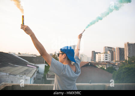 Männlichen Teenager halten bunte Rauchstäbe in der Luft über städtische Hintergrund Stockfoto