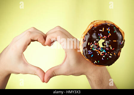 ein Donut und Herz Form von Händen isoliert auf gelb Stockfoto