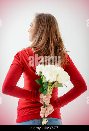 Schöne junge Frau hält hinter Rücken weißen Rosenstrauß. Stockfoto