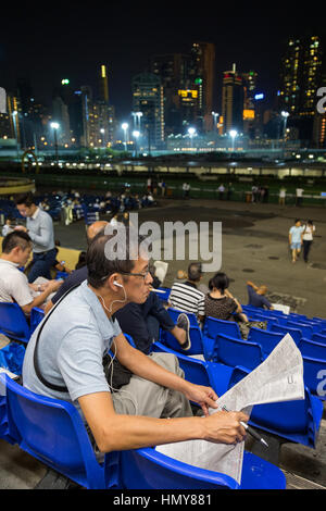 Chinesische Spieler Zigarette rauchen und lesen Zeitung und andere Leute an die Happy Valley Racecourse in Hong Kong, China, am Abend. Stockfoto