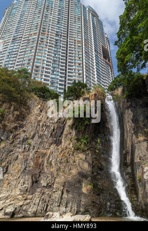 Steilen Felsen, Wasserfall und einem Hochhaus Wohnung Ansicht von unten am Wasserfall Bay Park in Hong Kong, China. Stockfoto