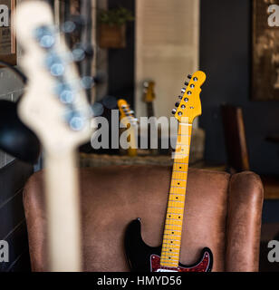 Detail der e-Gitarre Hals-schiefen Agaist Ledersitz. Anderen Hälse im Hintergrund und Vordergrund. Stockfoto