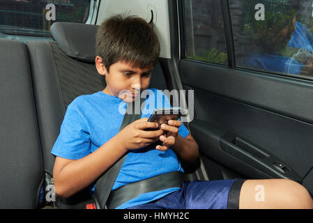 kleiner Junge mit Handy auf dem Rücksitz des Wagens Stockfoto