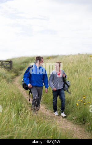 Vater und Sohn die Sandunes an den Strand hinunter. Tragen sie warme Bekleidung und Lächeln einander an. Stockfoto