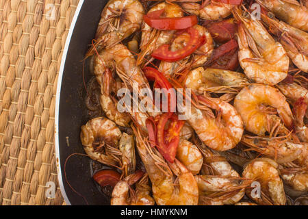 Frische Garnelen mit Tomaten und Zwiebeln gekocht / frisch gekochte Garnelen mit Tomaten und Zwiebeln serviert in einer Platte auf einem Hintergrund aus Holz (schwarz Keramik) Stockfoto