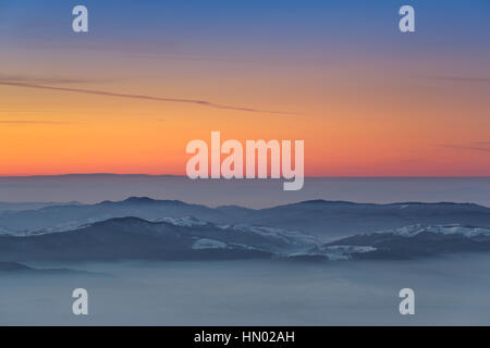 Idyllische Winterlandschaft mit Sonnenuntergang über neblige Täler der Karpaten Berge, Region Transsilvanien, Rumänien. Stockfoto