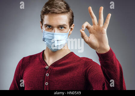 Gut aussehender Mann zeigt Ordnung Geste. Foto des gesunden Menschen trägt Schutzmaske gegen Infektionskrankheiten und Grippe. Health care Konzept. Stockfoto