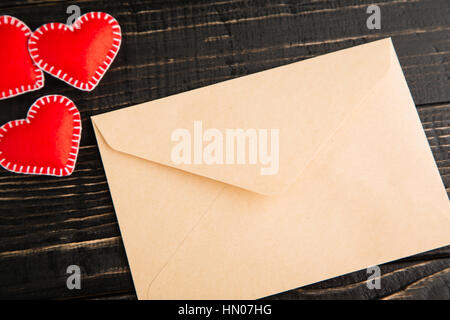 Craft Umschlag und rot handgefertigte Herzen aus Filz auf dem schwarzen rustikalen hölzernen Hintergrund. Flach zu legen. Valentinstag-Konzept, Textfreiraum, Ansicht von oben Stockfoto