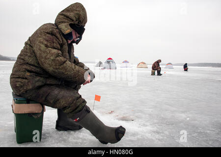 Ein russischer Mann auf kalten Wintertag wie er sitzt auf Eis Angeln an einem Fluß im Moskauer Gebiet. Eisfischen ist ein beliebtes Hobby in Russland Stockfoto