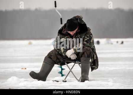 Ein russischer Mann auf kalten Wintertag wie er sitzt auf Eis Angeln an einem Fluß im Moskauer Gebiet. Eisfischen ist ein beliebtes Hobby in Russland Stockfoto