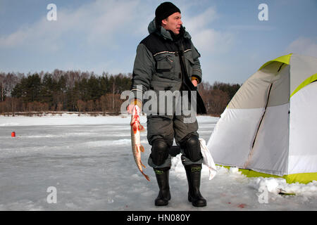 Ein russischer Mann auf kalten Wintertag wie er sitzt auf Eis Angeln an einem Fluß im Moskauer Gebiet. Eisfischen ist ein beliebtes Hobby in Russland Stockfoto