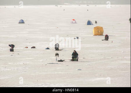 Ein russischer Mann auf kalten Wintertag wie er sitzt auf Eis Angeln an einem Fluß im Moskauer Gebiet. Eisfischen ist ein beliebtes Hobby in Russland Stockfoto