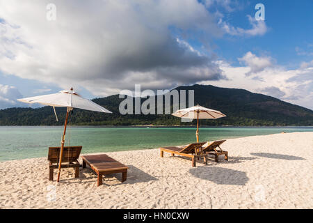 Idyllischen weißen Sandstrand mit Liegestühlen und Sonnenschirm in Koh Lipe Insel im Süden Thailands in der Andamanensee. Einer traditionellen Longtail Baot segelt in t Stockfoto
