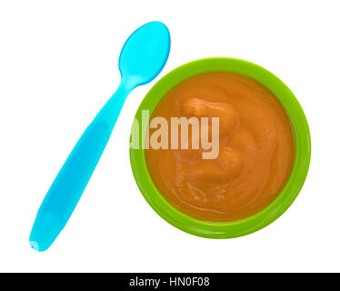 Draufsicht einer Portion Banane Karotte und Mango Babynahrung in einer grünen Schale mit einem blauen Löffel zur Seite isoliert auf einem weißen Hintergrund. Stockfoto